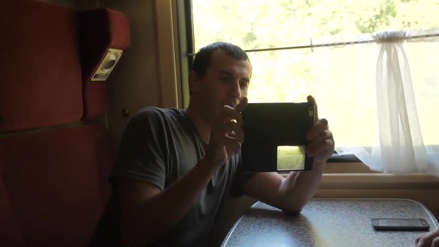man traveler Relaxing On Train Listening To Music and smiling through the pictures via social media. slow motion video . lifestyle uploading photo using cell phone while riding home by train wagon