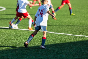 Boys in red white sportswear running on soccer field. Young footballers dribble and kick football ball in game. Training, active lifestyle, sport, children activity concept 