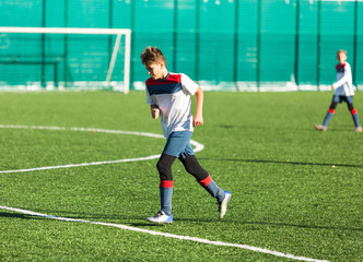 Boys in red white sportswear running on soccer field. Young footballers dribble and kick football ball in game. Training, active lifestyle, sport, children activity concept 