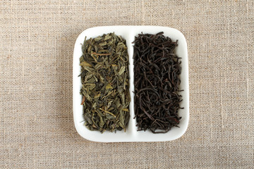 Green tea and black tea in square white saucer on rough linen cloth background