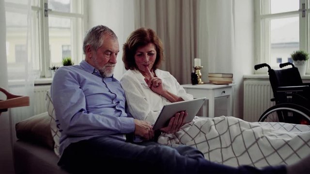 A senior couple with tablet at home, a husband spending time with his ill wife.