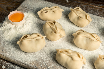 Uzbek national food manta, like dumplings, on a wooden board, lie in flour with an egg