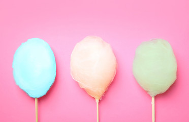 Sticks with different colorful yummy cotton candy on pink background, flat lay
