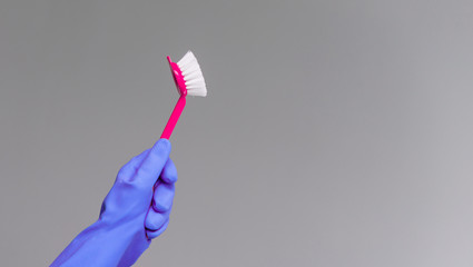 A hand in a rubber glove holds the dishwashing brush on a neutral background. The concept of bright spring, spring cleaning.