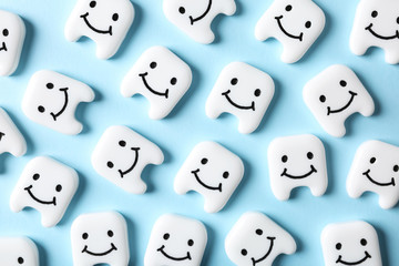 Many small plastic teeth with cute faces on color background, top view