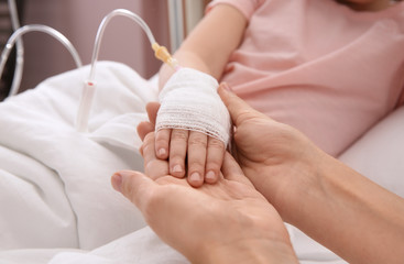 Doctor holding little child's hand with intravenous drip in hospital, closeup
