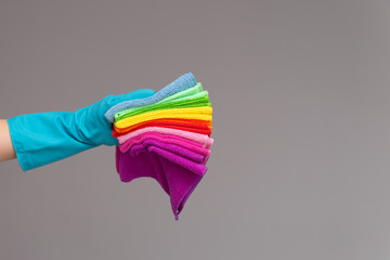 A hand in a rubber glove holds a set of colored microfiber cloths on a neutral background. The concept of bright spring, spring cleaning.