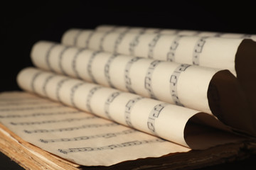 Old wrapped sheets with music notes on black background, closeup