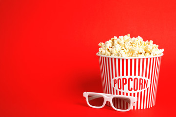 Bucket of fresh tasty popcorn and glasses on color background, space for text. Cinema snack