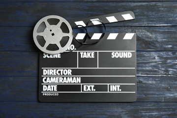 Clapperboard and reel on wooden background, top view. Cinema production