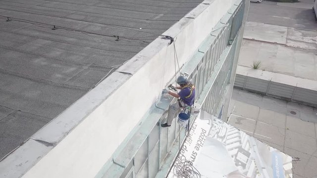 Descending aerial shot down to high altitude climber working on office building maintenance secured with ropes & rigging.