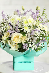 Beautiful bouquet of flowers in decorative crate on table against light background