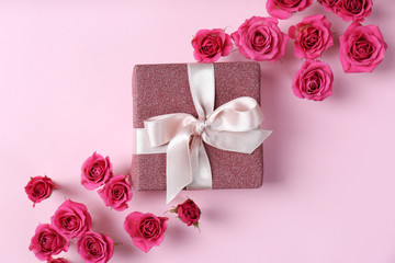Beautiful roses and gift box on color background, top view