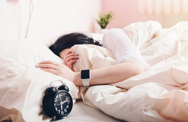 girl on white bed with alarm clock and smart watch on hand