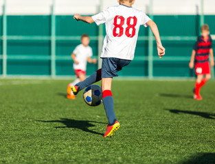 Boys in red white sportswear running on soccer field. Young footballers dribble and kick football ball in game. Training, active lifestyle, sport, children activity concept 