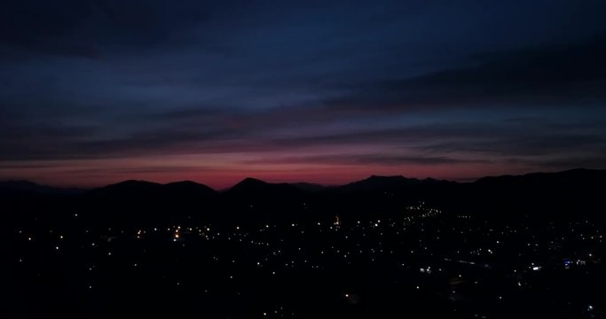 After the sun has set over a rural town with a red sky DRONE slow left