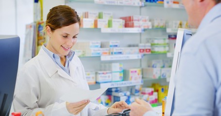 Portrait of young woman pharmacist handing over prescribed medicines to a patient in drugs store....