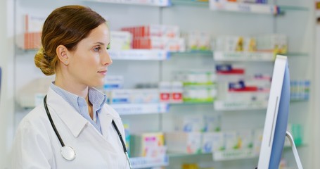 Portrait of young woman pharmacist searching medicine for a patient  in computer in a drugs store. Shot in 8K. Concept of profession, medicine and healthcare, medical education, pharmaceutical sector