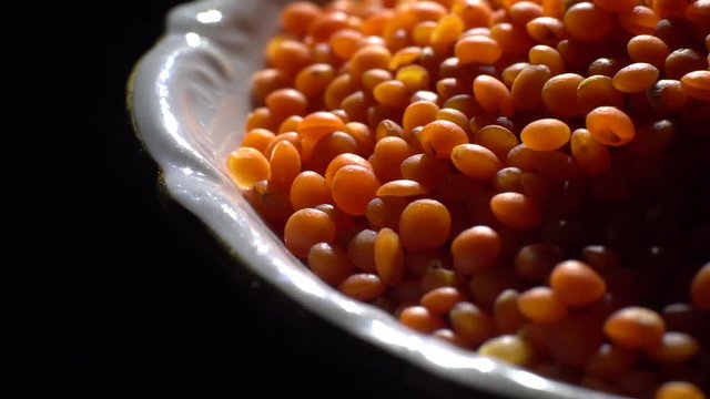 Lentils. Heap of raw uncooked red lentils in bowl in rotation.  Red Chief Lentils, petite crimson lentils - Close up. Food background. black background, studio shot. Healthy organic food diet concept
