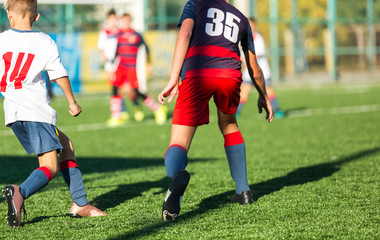 Boys in red white sportswear running on soccer field. Young footballers dribble and kick football ball in game. Training, active lifestyle, sport, children activity concept 