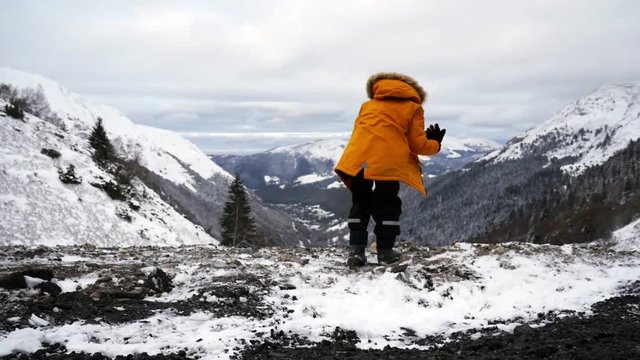 amazing video of little boy in yellow coat dancing and jumping with excitement looking at the mountains covered in snow. slow motion
