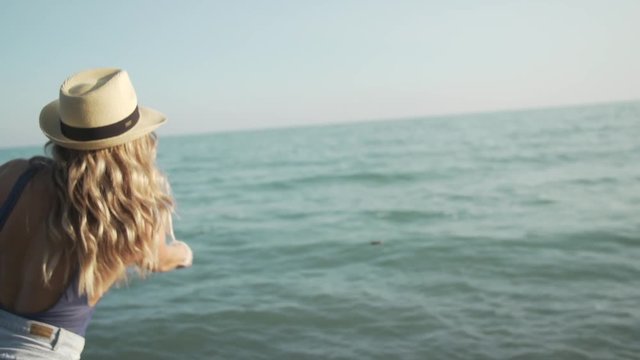 A girl throws a rock into the water at sunset.