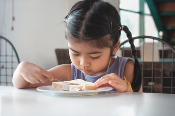 Asian children are making butter bread with knife .