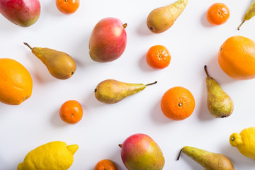 Pears, mango, oranges, lemon and mandarins scattered on white background, top view
