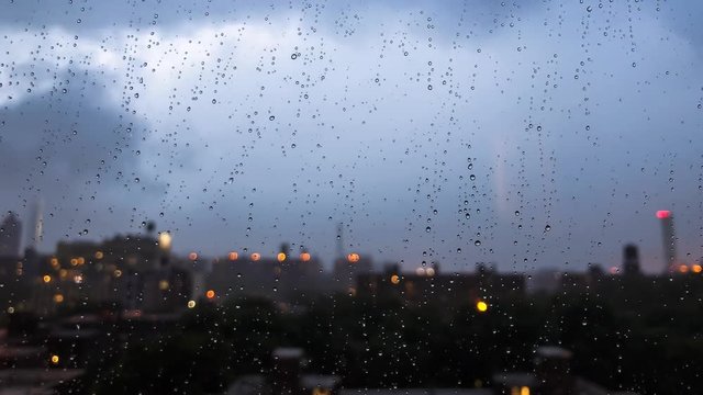 Raindrops gather on windowpane while the evening lights of New York City come up in the background.