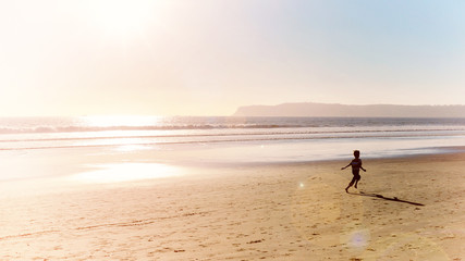 Fototapeta na wymiar ocean beach at sunset and boy running along shore of pacific ocean seaside at san diego city in california usa retro vintage style photo vacation happy childhood panoramic scene
