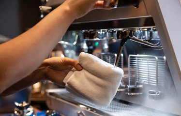 Hand of barista cleaning milk frother of coffee machine to be ready for milk frothing at coffee shop