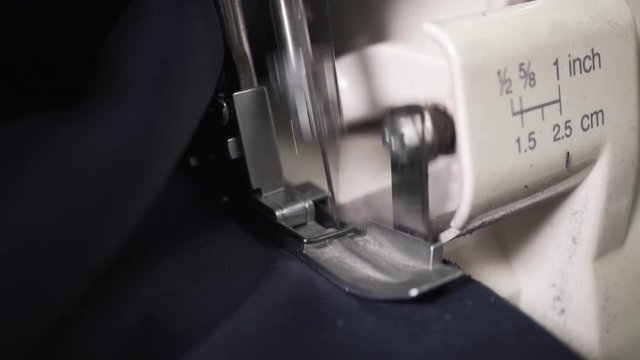 Seamstress sews clothes made of blue cloth on a sewing machine. Work by the light of the built-in hardware lamp. Steel needle with looper and presser foot close-up