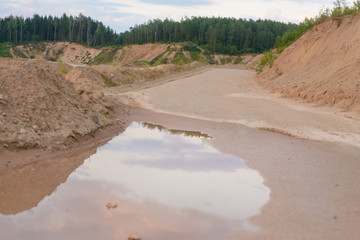 a long road of rubble with puddles along the quarry and forest