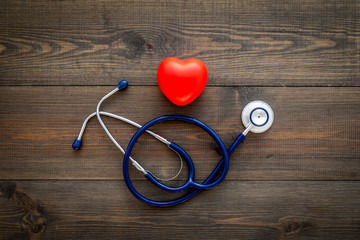 Heart health, health care concept. Stethoscope near rubber heart on dark wooden background top view...