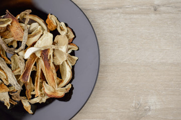 diet healthy vegetarian meal: sun-dried boletus on a black plate on a wooden table to the right in the center; a source of protein and micronutrients