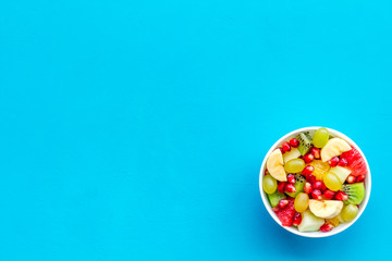 Light healthy breakfast or appetizer. Fruit salad with apple, kiwi and pomegranate in bowl on blue background top view copy space