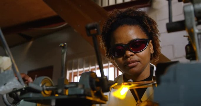 Attentive black female worker blowing glass in glass factory 4k