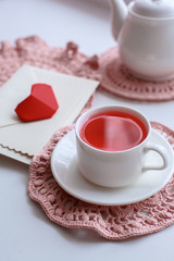 Cup of scented pink tea on crocheting napkin, teapot and envelope on windowsill. Valentines day. Romance Good morning