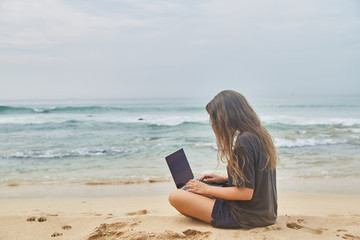 Young girl working at the computer on the beach. The freelancer working on the beach.