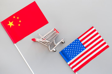 USA and China trade war. American and chinese flags near shopping chart on grey background top view copy space