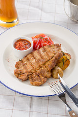 Grilled pork steak with potato wedges, tomatoes and ketchup on white plate on textile background