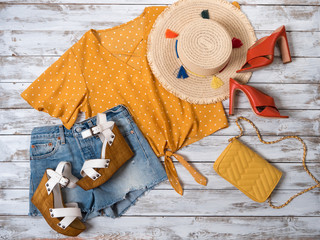 Womens clothing, accessories, footwear (heels shoes, wedges sandals, denim shorts, yellow blouse, bag, straw hat). Fashion outfit, spring summer collection. Shopping concept. Flat lay, view from above