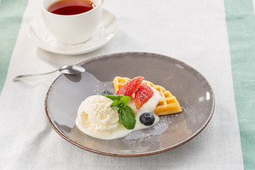Fresh belgian waffles with ice cream and berries and cup of tea served on the table