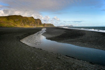 Black sand beach with small stream reflection in Vik, Southern Iceland.