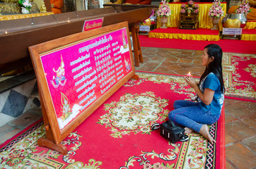 Thai woman sitting respect praying big reclining buddha statue in ubosot or church at Wat Phra Non Chakkrasi Worawihan in Sing Buri , Thailand.