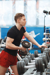 Young man exercising with dumbbells in a gym, focus on the weights.