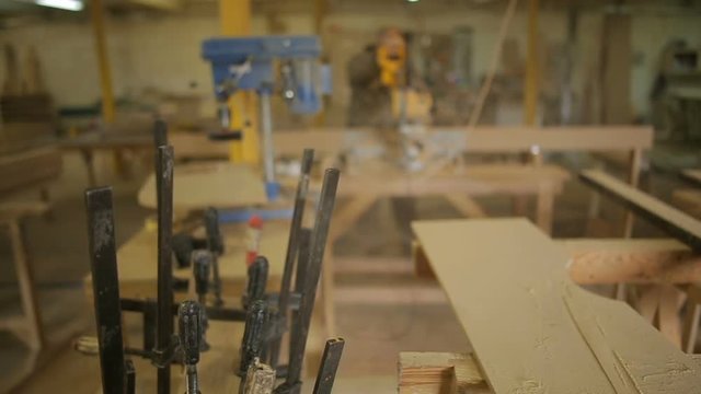 focus on F-clamps or bar clamps and Carpenter or Joiner works in workshop of furniture on the background