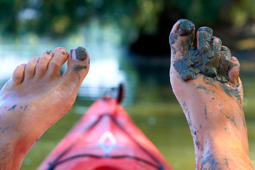 Men's bare feet in mud on red kayak