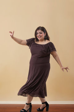 Fat woman in a long brown dress dancing on high heels	
