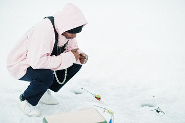 Fototapeta na wymiar African american fisherman with fishing rod sitting on frozen sea. Winter fishing.